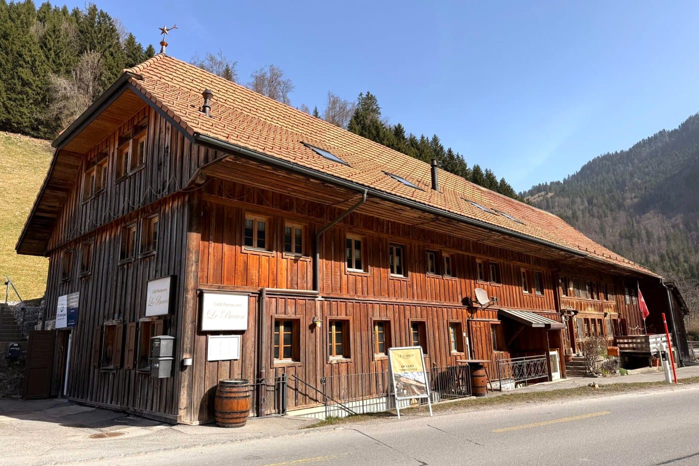 La bâtisse de bois du Baron et son toit de tuiles, au bord de la route, sous un ciel bleu