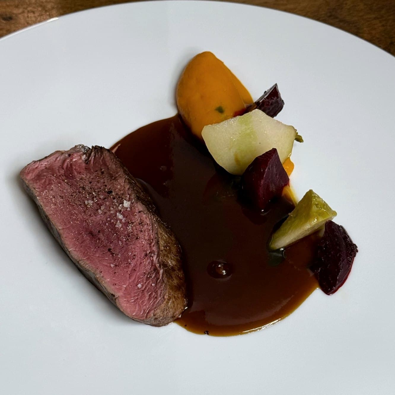 Viande rosée, jus et légumes racines sur une assiette blanche
