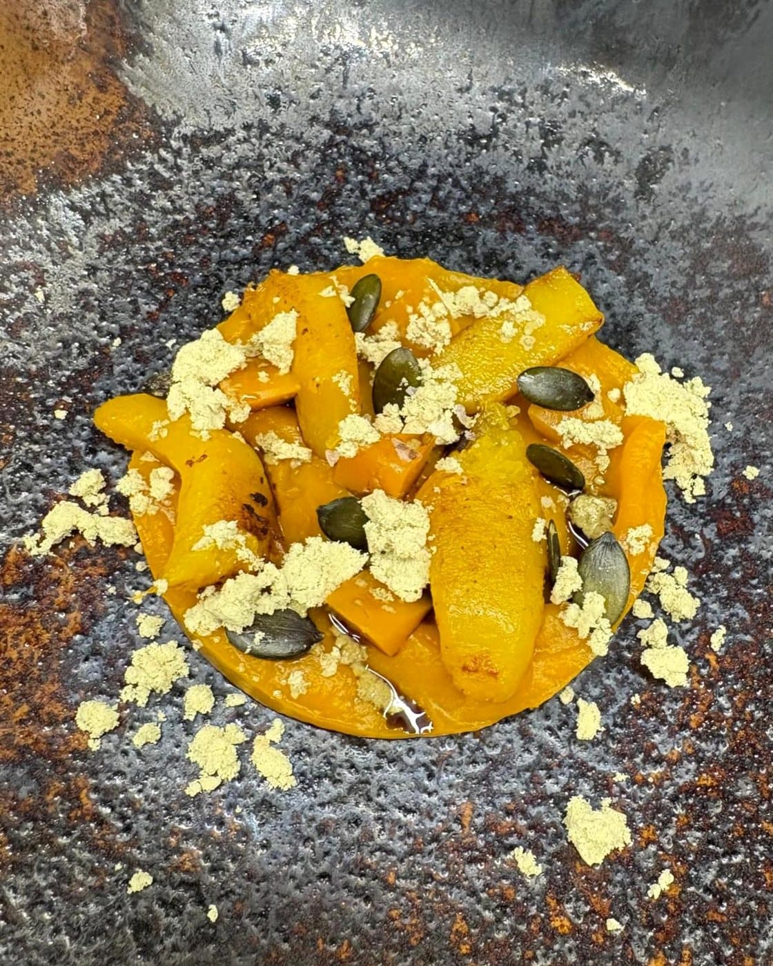 Courge rôtie, graines de courge et poudre de fromage sur une assiette en grès sombre