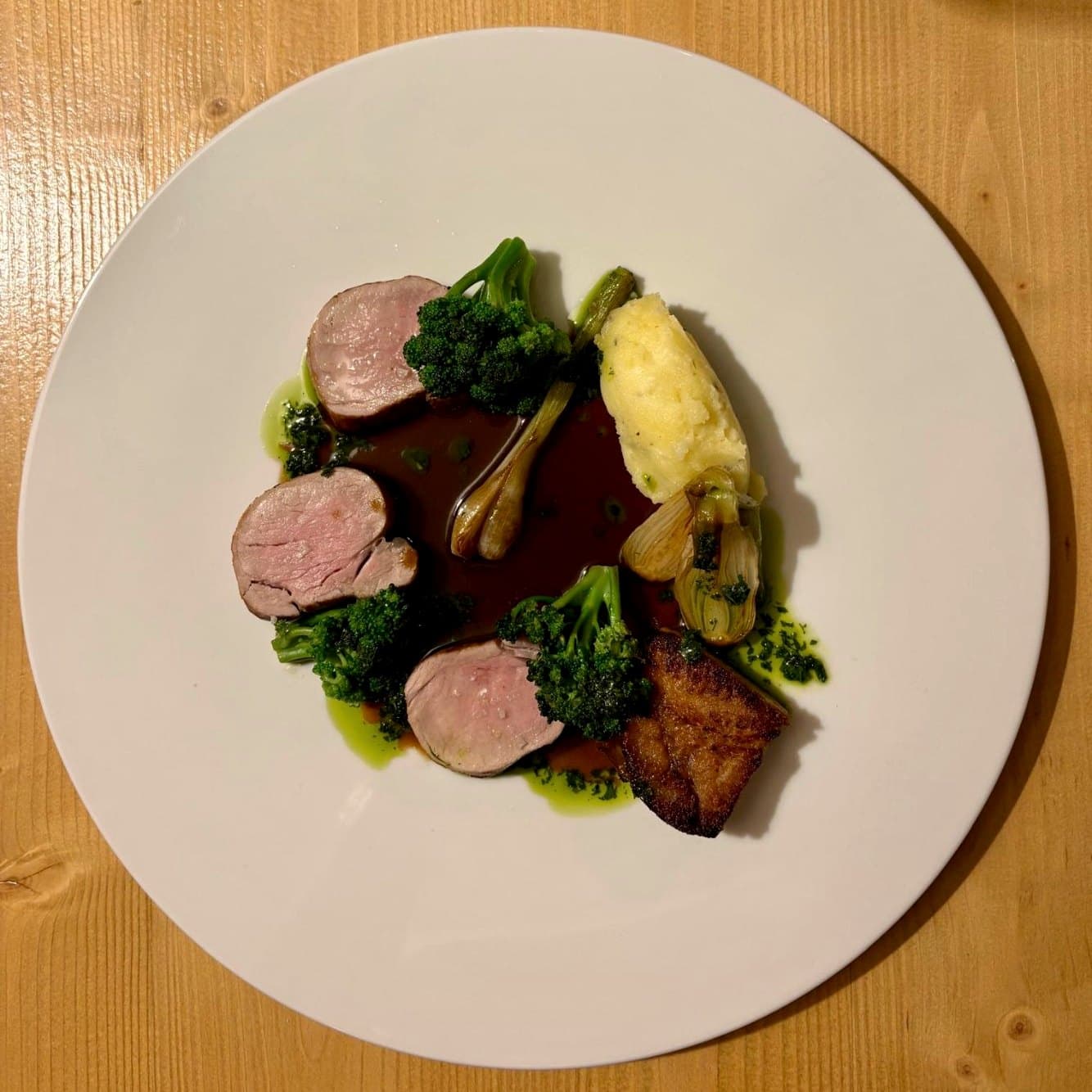 Médaillons de viande, brocolis et sauce sur une assiette blanche posée sur le bois
