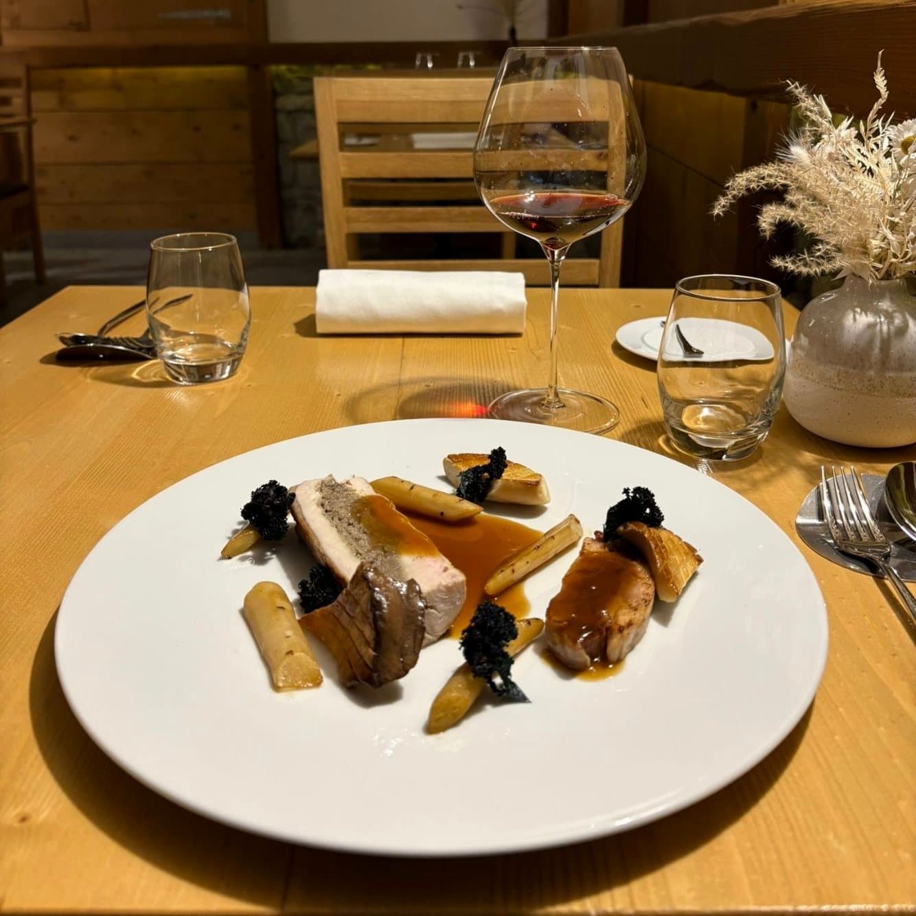 Une assiette servie sur une table de la salle boisée, verres et bouquet séché